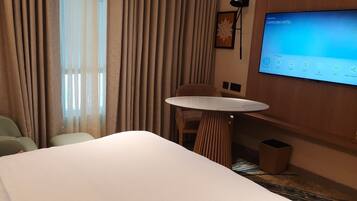 A hotel room with a bed, a small round table, a sofa, and a TV screen displaying a welcome message.