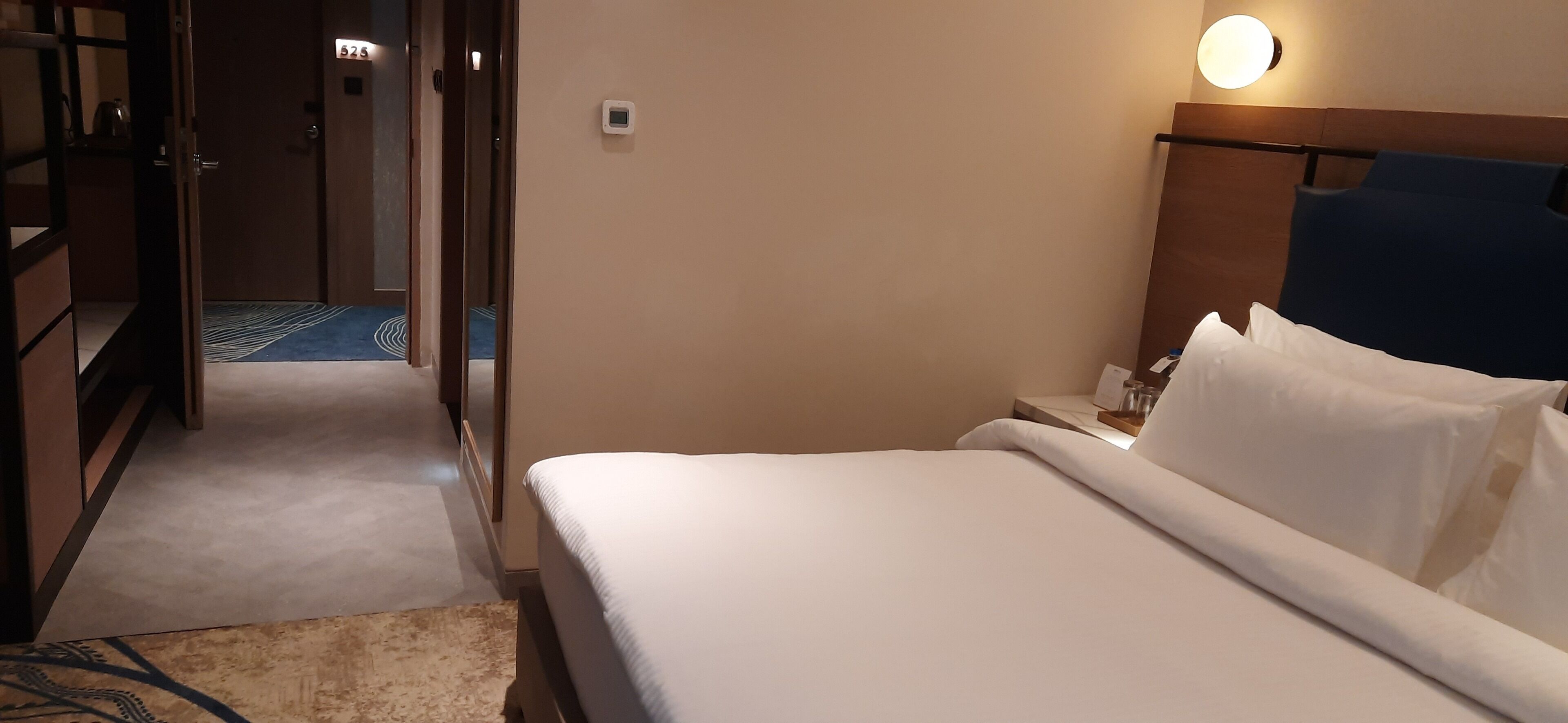 Una habitación de hotel con cama, mesita de noche y lámpara en la pared.