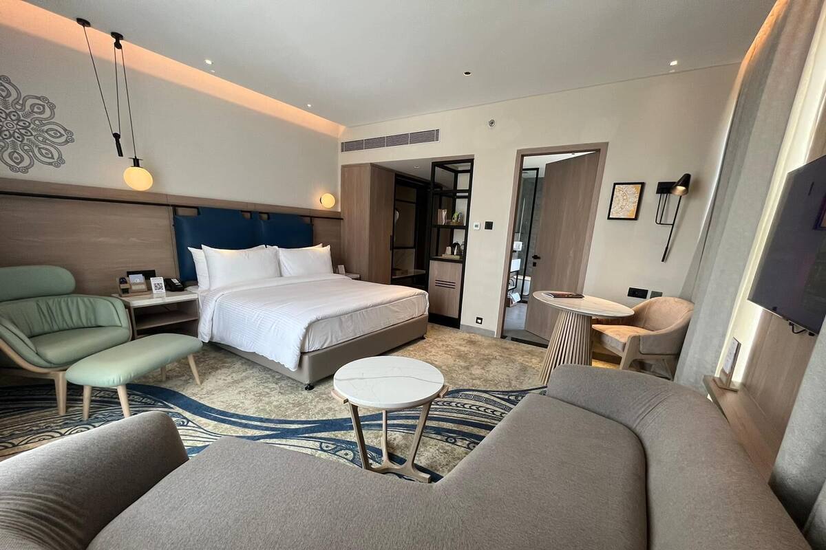 Quarto de hotel moderno com uma cama grande, um sofá, uma mesa redonda pequena e uma televisão.