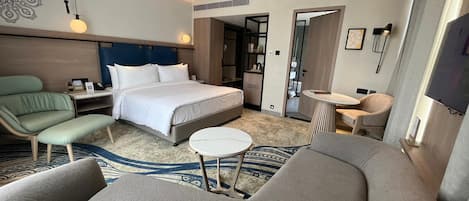 Una habitación de hotel moderna con una cama grande, un sofá, una pequeña mesa redonda y un televisor.