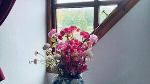 A room with a window, a vase with flowers, and some books on a table. - The Stables Cottage (Darnick)