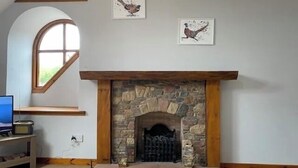 A room with a stone fireplace, a wooden mantel, and two wall-mounted bird paintings. - The Stables Cottage (Darnick)