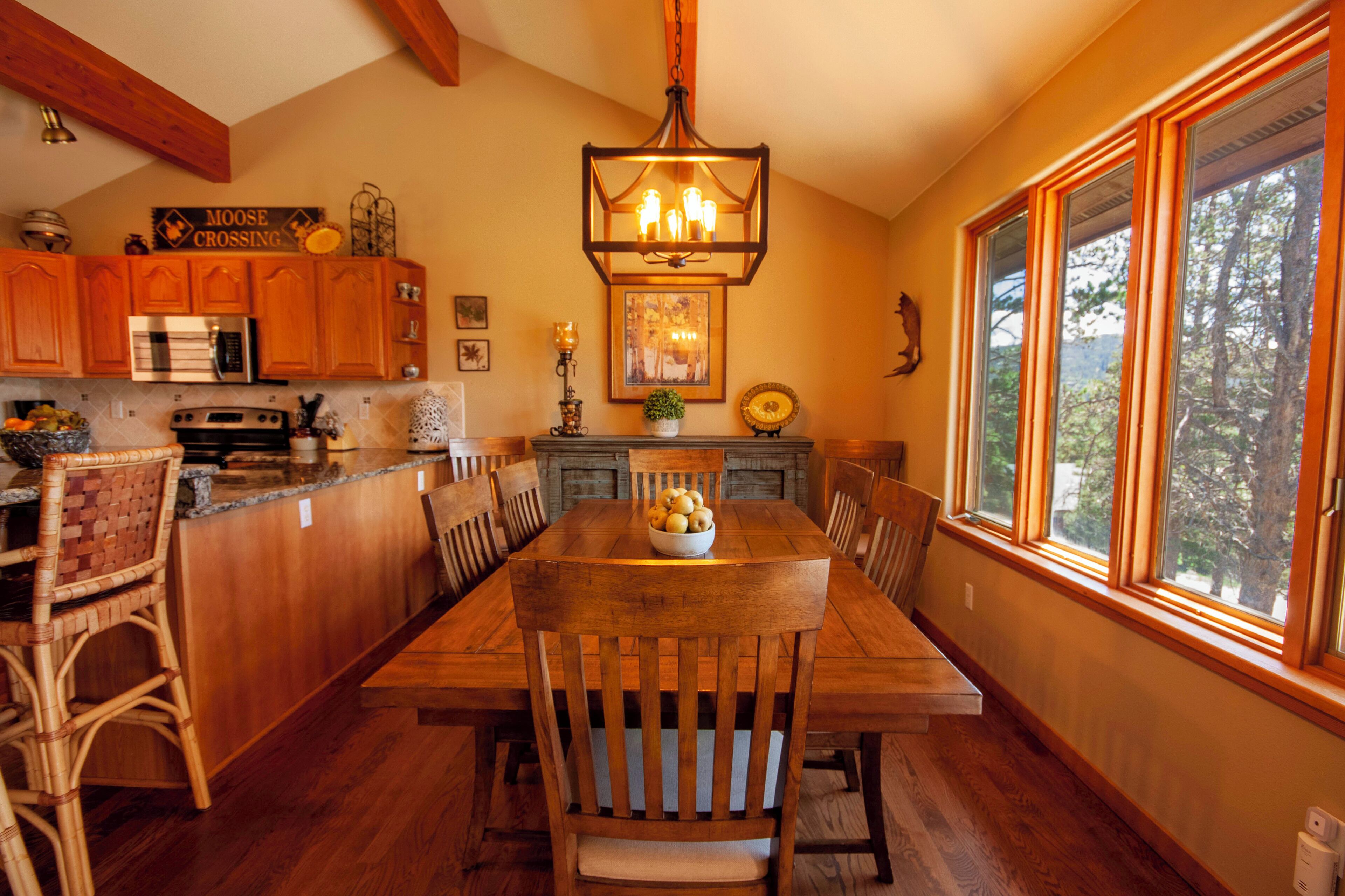 A wooden dining table with chairs, a chandelier, and a window with a view of trees.