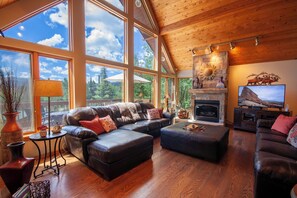 A spacious living room with a fireplace, leather sofas, and large windows offering a view of the outdoors. - Moose Crossing (Breckenridge)