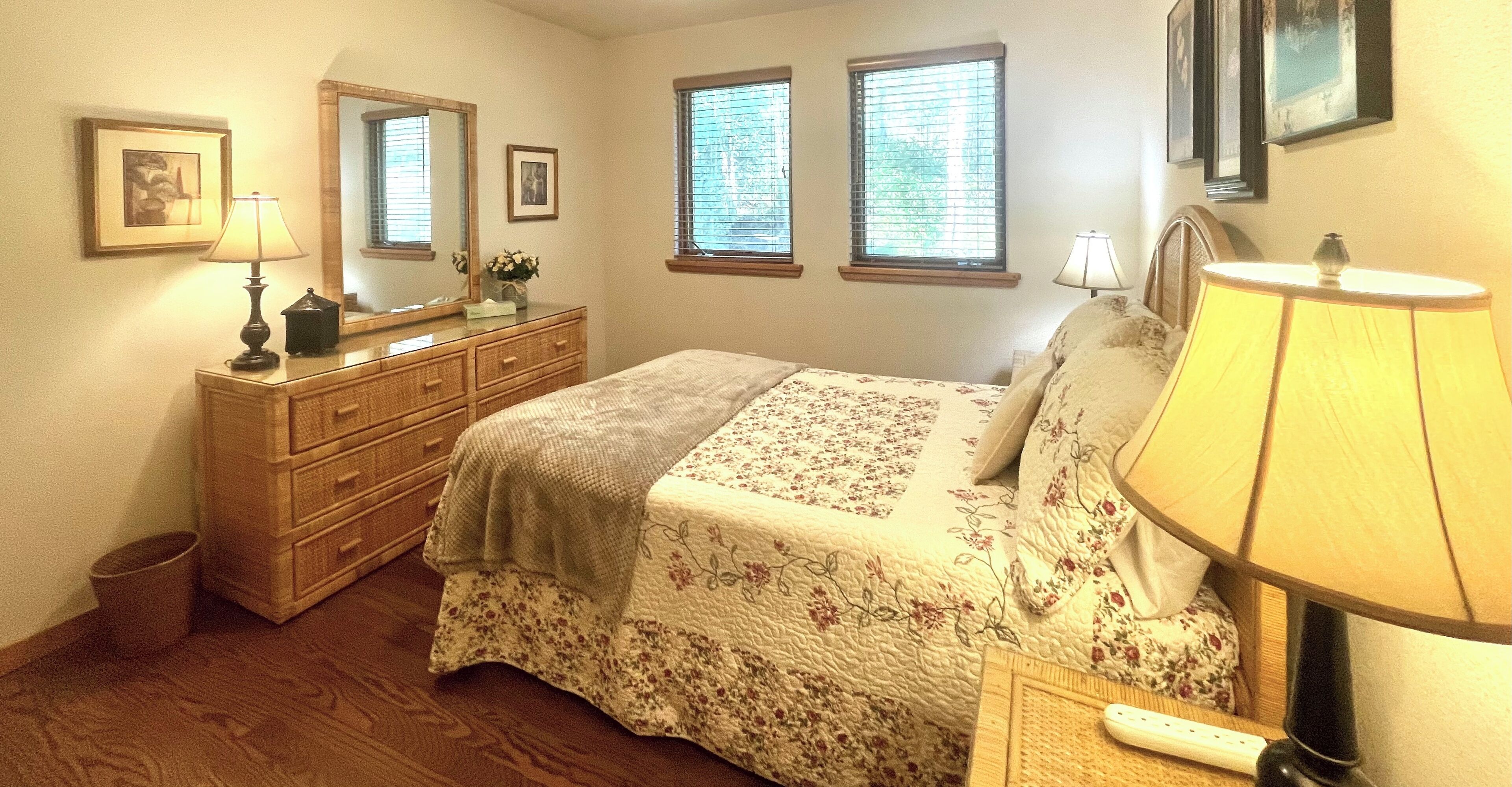 A bedroom with a bed, dresser, mirror, and two windows.
