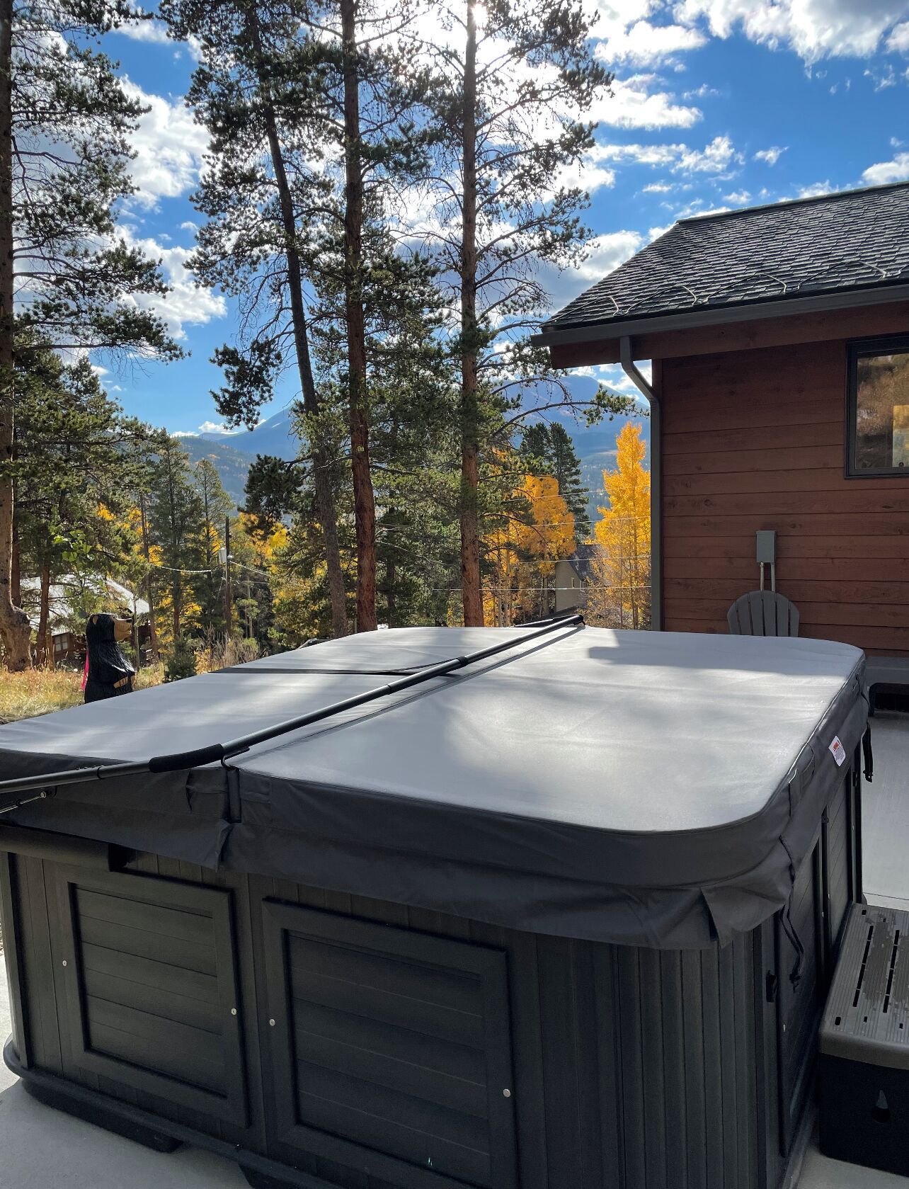 A hot tub with a cover, a wooden deck, and a view of trees and a mountain in the background.