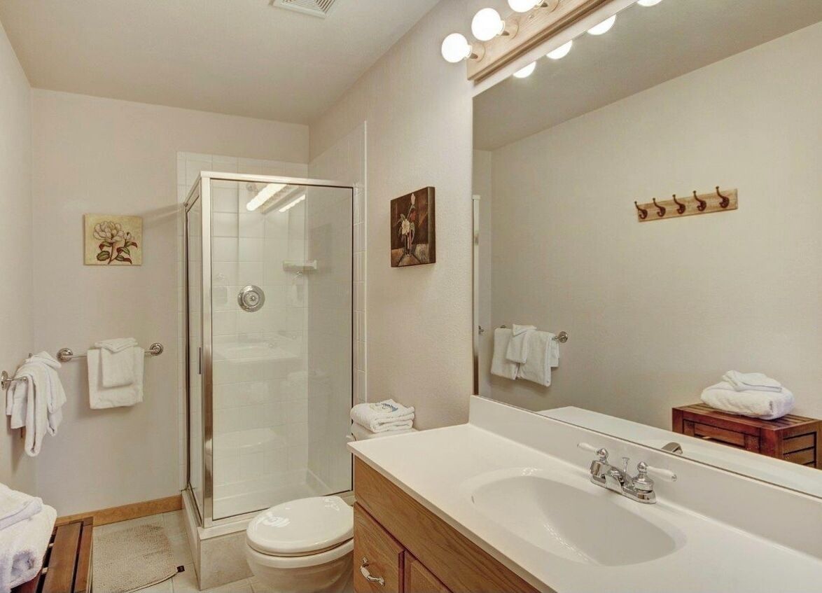 A modern bathroom with a glass shower enclosure, a large mirror, and a white sink.