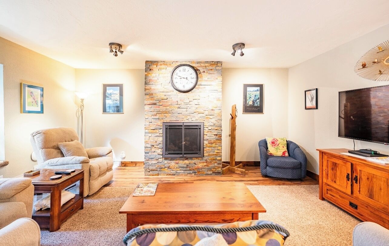 A living room with a stone fireplace, a large flat-screen TV, and comfortable seating.