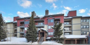 A multi-story hotel with a central entrance, balconies, and a covered parking area.