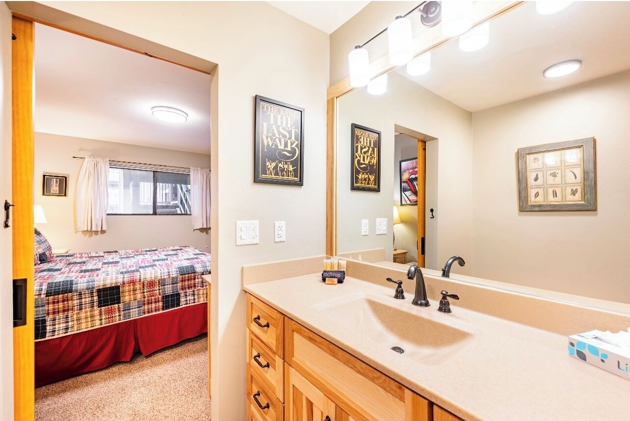 A bedroom with a bed, a bathroom with a sink and mirror, and a window with curtains.