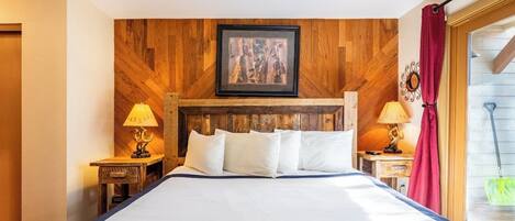 A hotel room with a wooden headboard, a large bed with white linens, two bedside tables with lamps, and a framed picture above the bed.