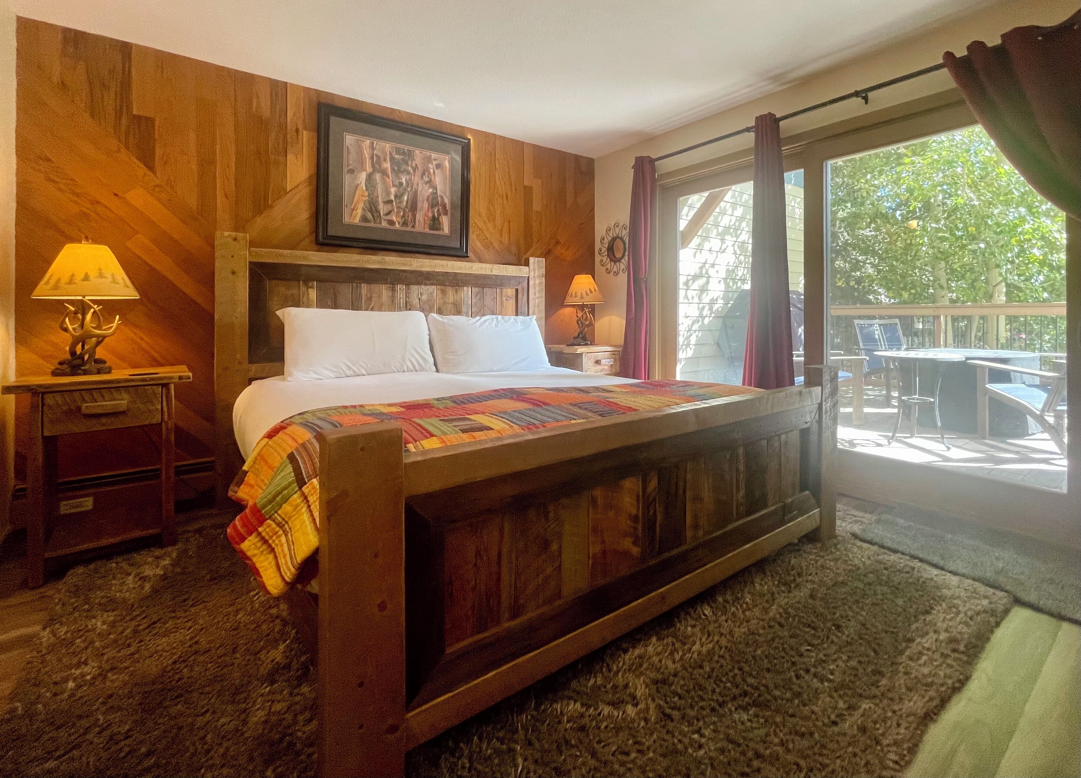Une chambre avec un lit en bois, une grande fenêtre avec des rideaux, une vue sur l’extérieur et un tableau accroché au mur.