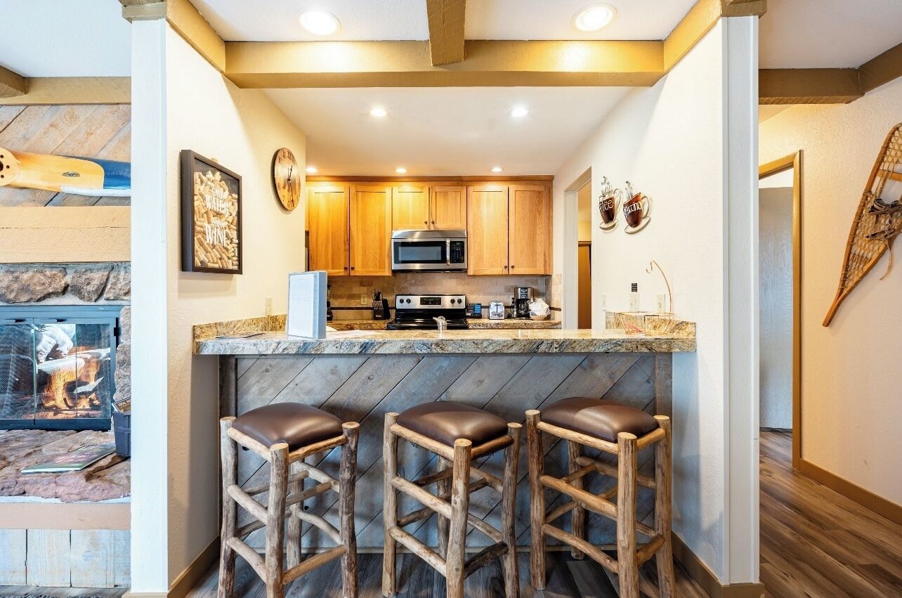 A kitchen with wooden cabinets, a microwave, a coffee machine, and a bar area with stools.