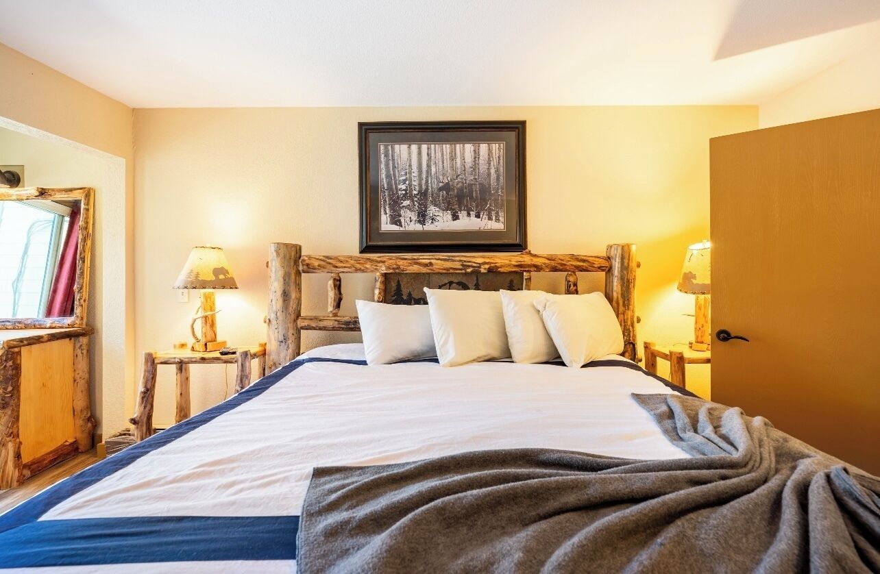 A bedroom with a wooden headboard, a framed picture above the bed, and bedside lamps.