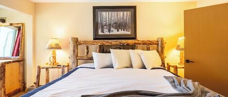A bedroom with a wooden headboard, a framed picture above the bed, and bedside lamps.