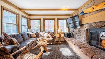 A cozy living room with a fireplace, large windows, a sofa set, and a stone accent wall.