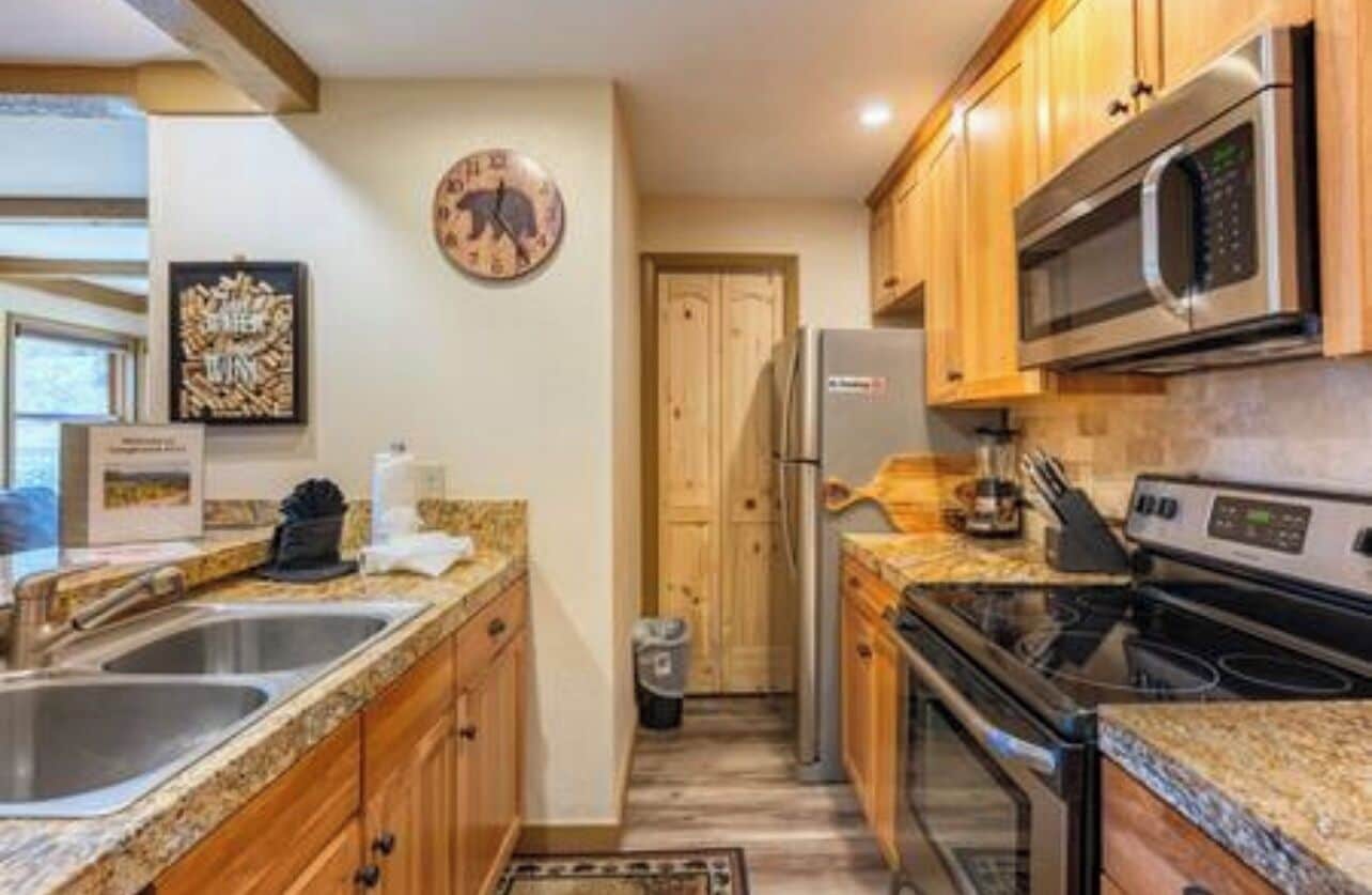 A compact kitchen with wooden cabinets, a stainless steel microwave, a refrigerator, and granite countertops.