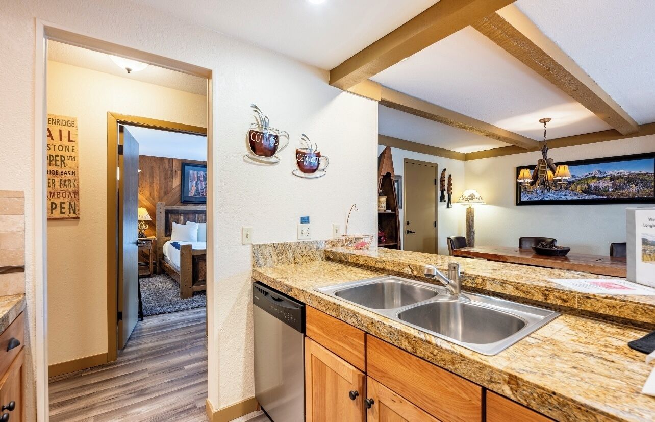 A modern kitchen with granite countertops, a double sink, wooden cabinets, and a dishwasher.