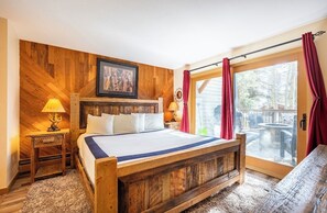 A wooden-framed bed with white linens, a wooden headboard, and a large window with red curtains. - Longbranch #111 (Breckenridge)