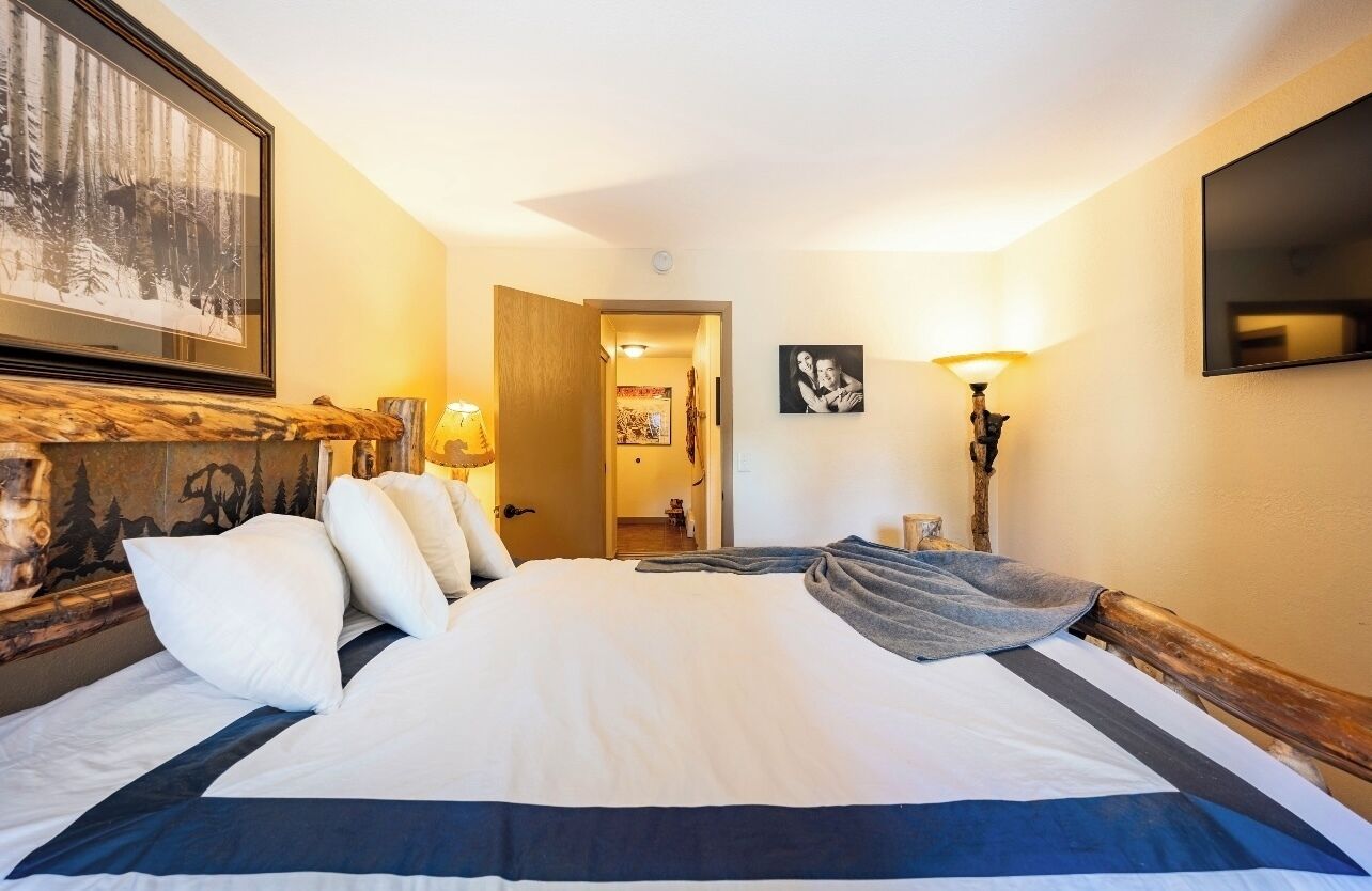 Quarto de hotel com uma cama grande, cabeceira de madeira, lareira e um quadro na parede.