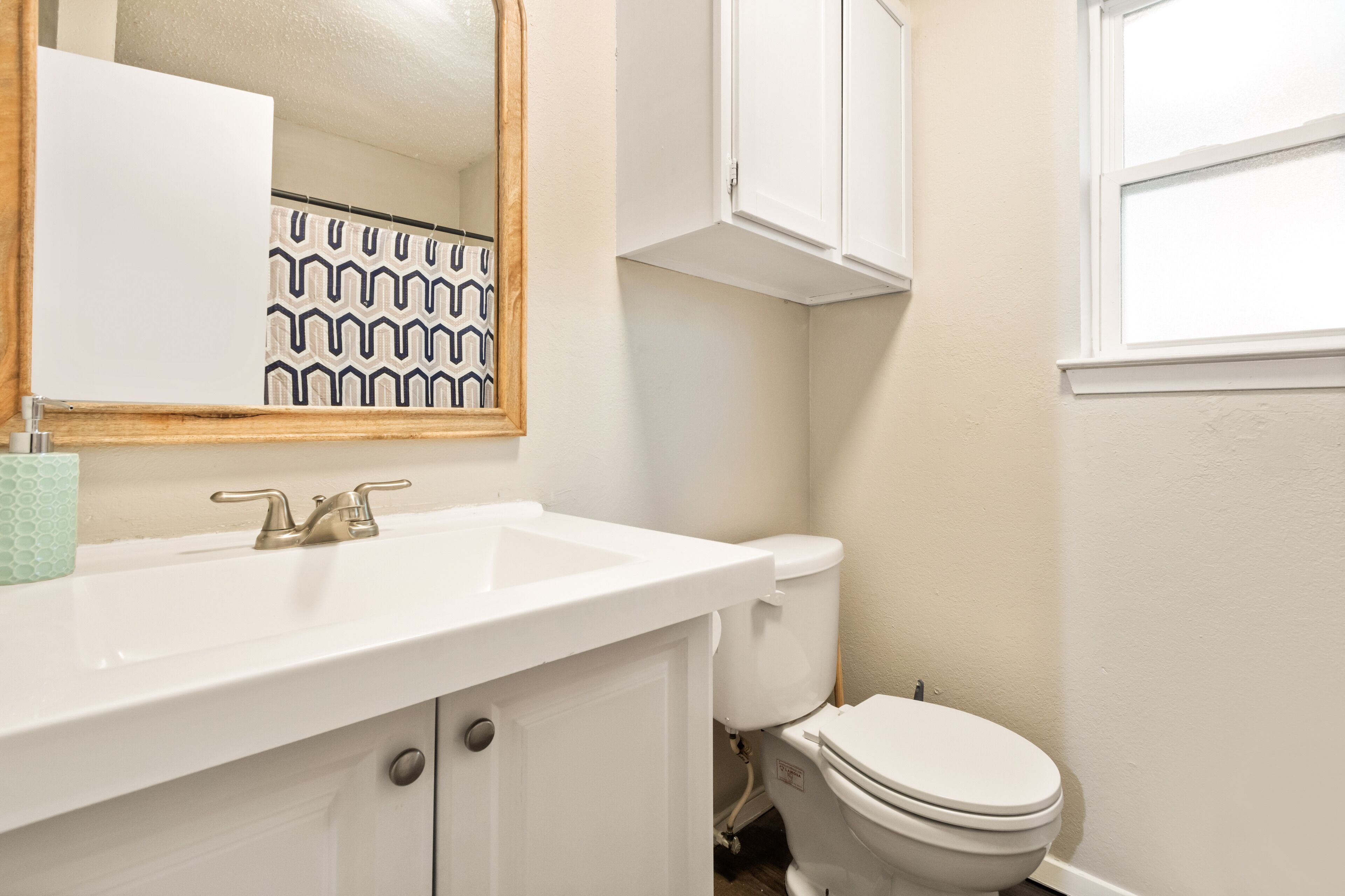 A bathroom with a white sink, a mirror, a toilet, and a window.