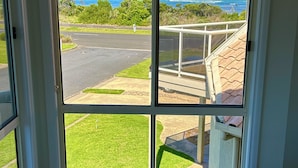 A room with a large window offering a view of a road and greenery, a small table, and a chair with a patterned cushion. - Ongermein, double story beach house a stone throw from the Indian Ocean.  (Port Macdonnell)