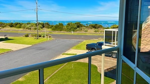 A balcony with a view of a road, a parked vehicle, and a distant body of water. - Ongermein, double story beach house a stone throw from the Indian Ocean.  (Port Macdonnell)