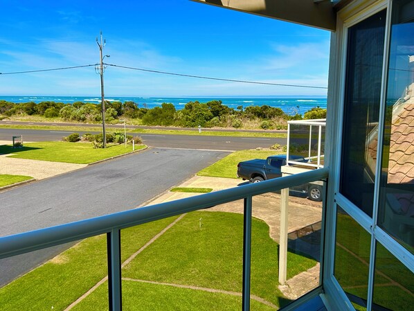 A balcony with a view of a road, a parked vehicle, and a distant body of water.