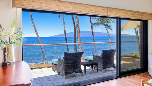 A room with a large sliding glass door leading to a balcony with wicker furniture and a view of the ocean.