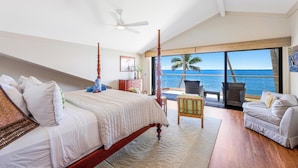 A bedroom with a large bed, a ceiling fan, and a view of the ocean.