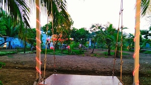 A swing set in a garden with palm trees and a dirt ground. - Starlight Resort (Alibag)