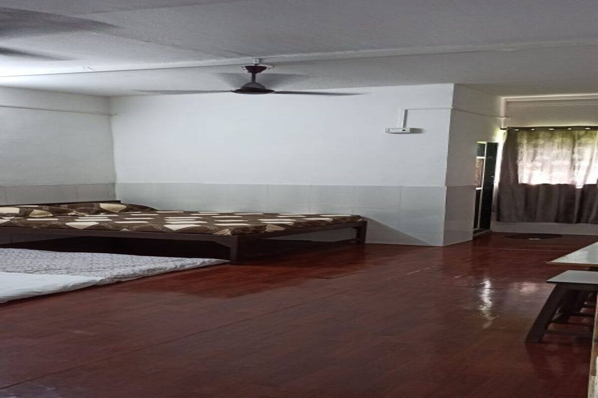 A room with a bed, a ceiling fan, a small table, and a door leading to another room.