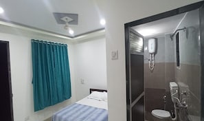 A hotel room with a bed, a bathroom with a shower, and a toilet. - Starlight Resort (Alibag)