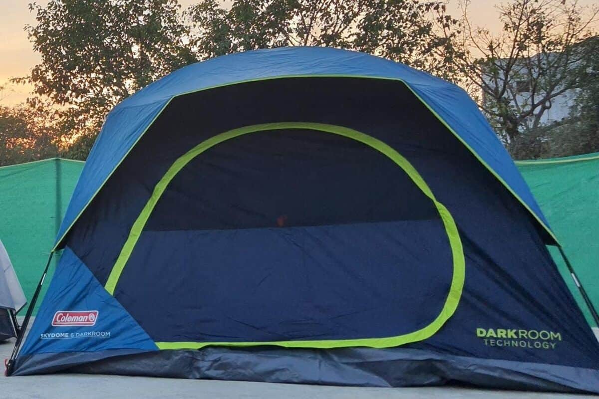 A Coleman tent with a darkroom technology feature, set against a backdrop of trees and a clear sky.