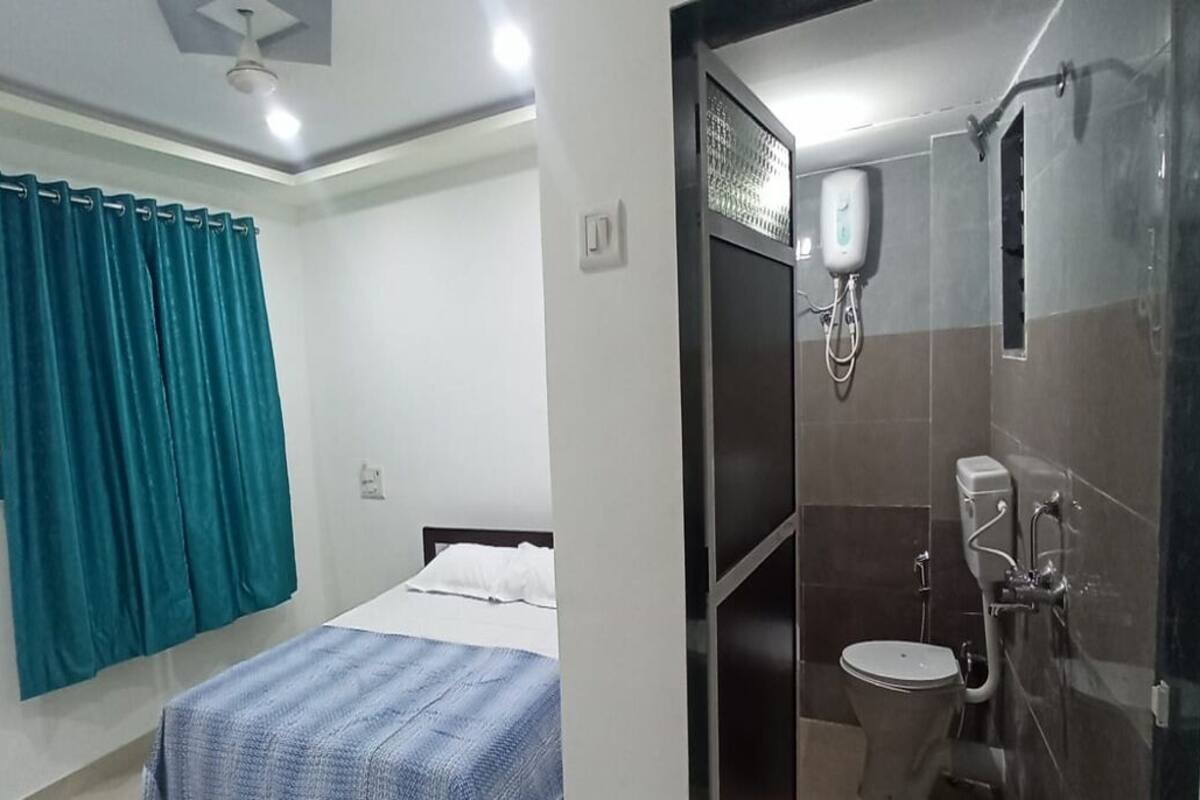 A bedroom with a bed, a bathroom with a toilet and shower, and teal curtains.