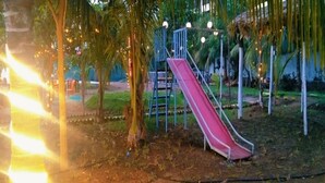 A playground with a red slide and a blue climbing structure, surrounded by palm trees and string lights. - Starlight Resort (Alibag)