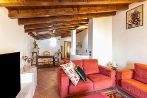 A living room with a red sofa, wooden ceiling beams, a TV, and a dining area with a table and chairs.