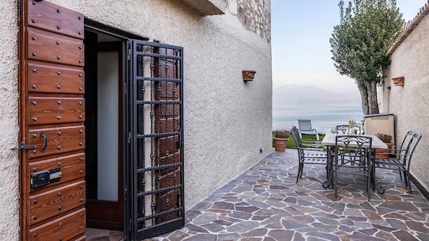 A stone patio with a table and chairs, a wooden door with a metal gate, and a view of the sea. - Villa "L'antica Lugana" with lake view, balconies, and Wi-Fi (Sirmione)