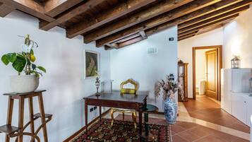 Una stanza con soffitto in legno, un tavolo da pranzo, una sedia, una pianta in vaso, un vaso e un pavimento piastrellato.