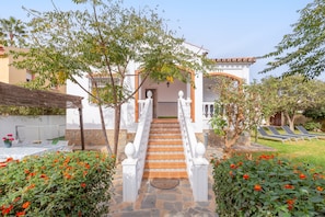 A building with a staircase leading to a covered entrance, surrounded by greenery and a pool area.