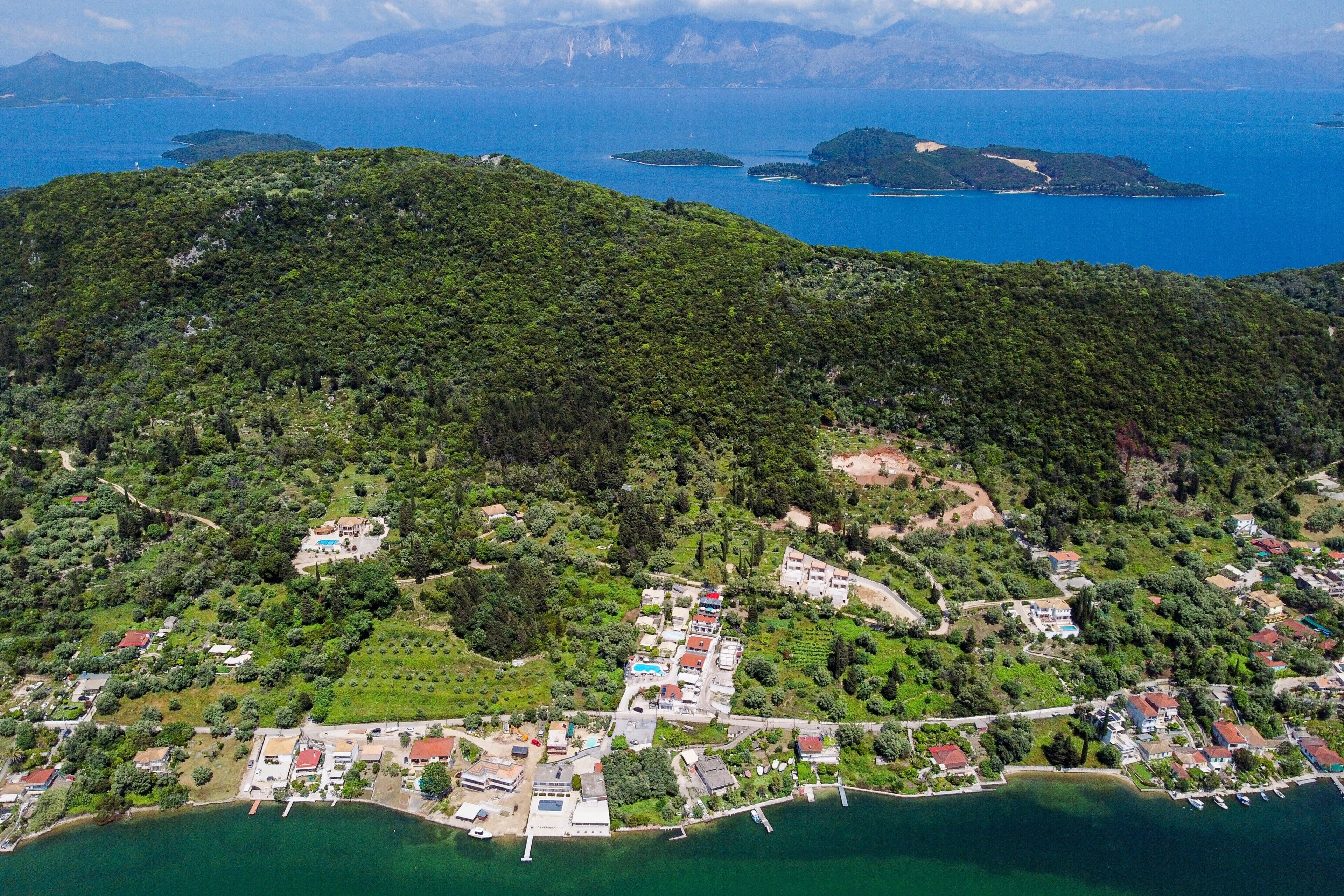 An aerial view of a coastal area with dense greenery, a marina, and scattered buildings.