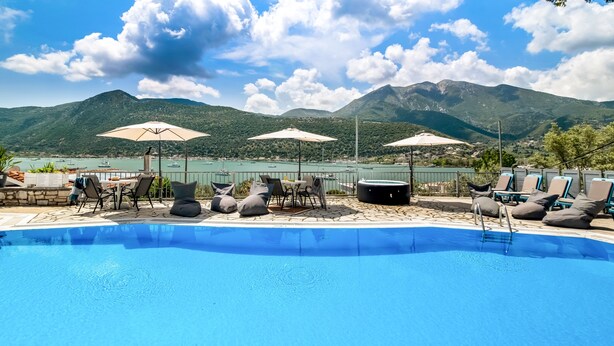 A swimming pool with lounge chairs and umbrellas, surrounded by mountains and a body of water. - Studio Apartment 'Chakalaka with Sofa Bed 15' with Sea View, Wi-Fi and Air Conditioning (Leykada)