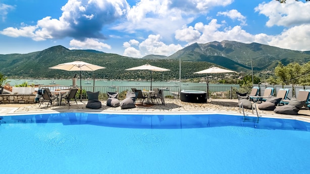 Una piscina amb gandules i ombrelles, envoltada de muntanyes i una massa d'aigua.