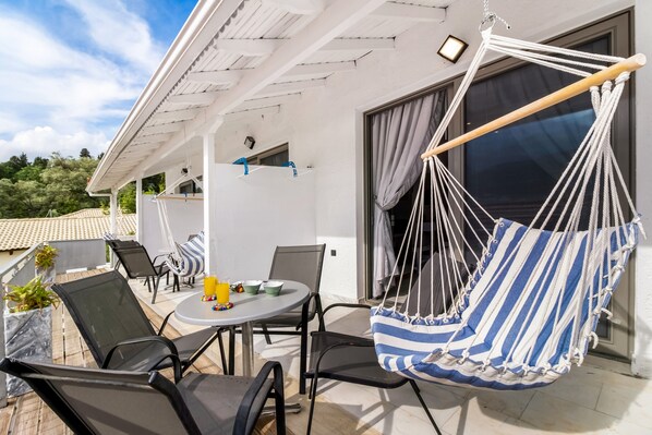 A patio with a table, chairs, a hanging chair, and a view of the surrounding area.