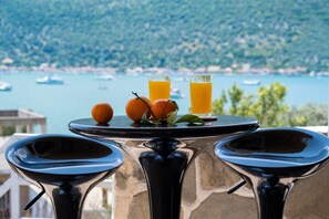 A table with two glasses of orange juice and oranges, overlooking a body of water with boats.