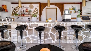 Zona de bar amb parets de pedra, tamborets negres i diverses ampolles i vasos a les prestatgeries.