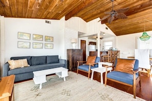 A spacious living area with a wooden ceiling, a gray sofa, a blue armchair, and a white coffee table.