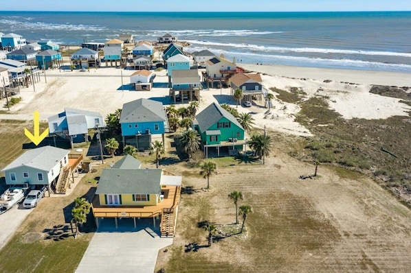 An aerial view of a coastal residential area with houses, a beach, and a clear view of the ocean.
