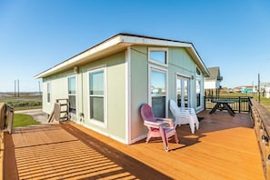 A small, single-story building with a wooden deck and two chairs.