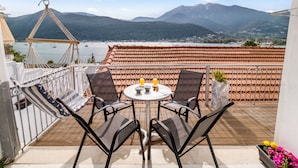 Terraza con vistas a montañas y agua, que incluye una hamaca, dos sillas, una mesa con bebidas y una planta en maceta.